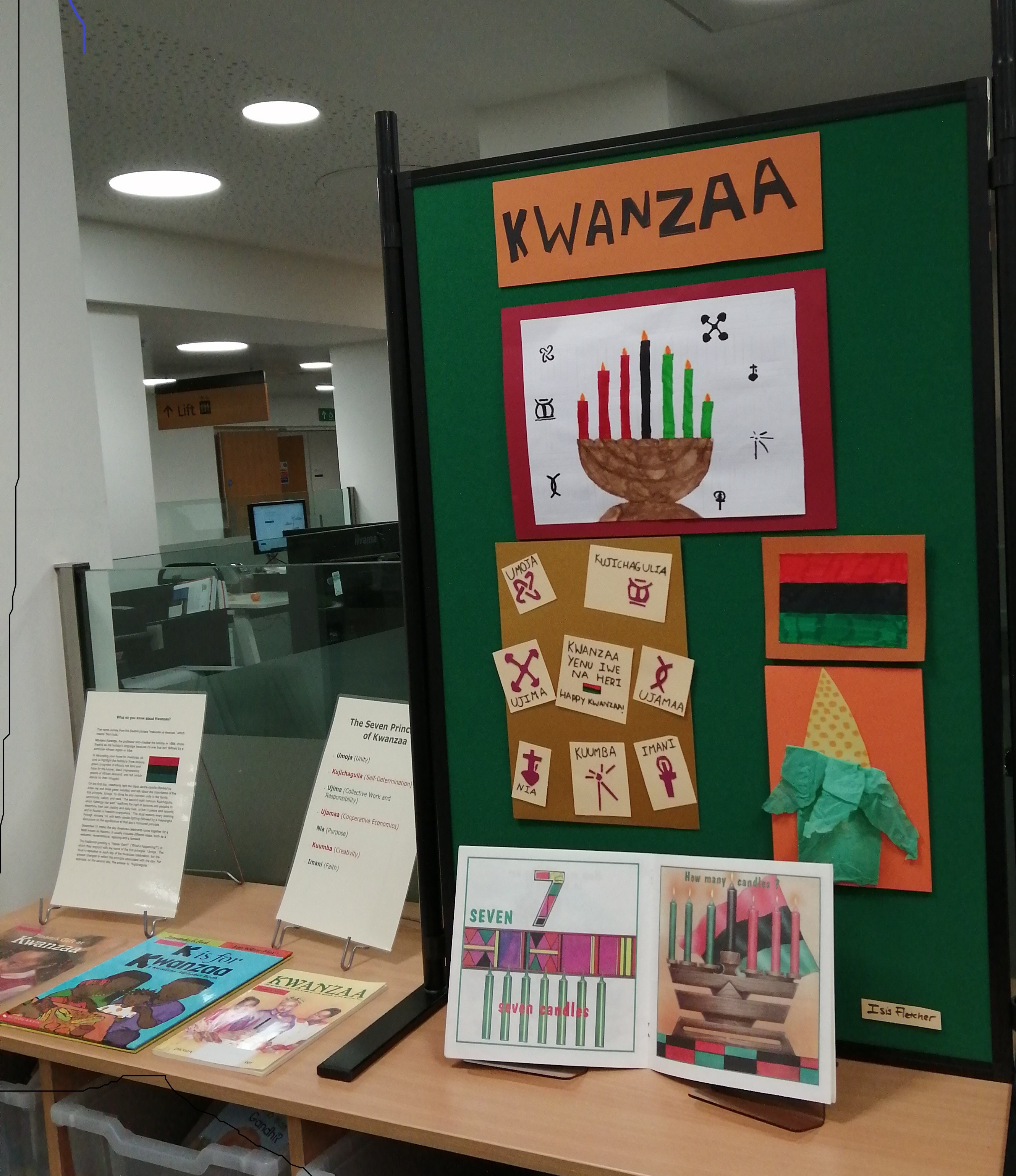 Kwanzaa  display in library including artwork of 7 branched candle and symbols of the 7 principles, books and information cards.