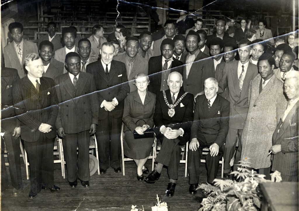 A group of delegates and guests to the 5th Pan African congress sit and stand in rows with the Mayor of Manchester sat in the centre of image.
