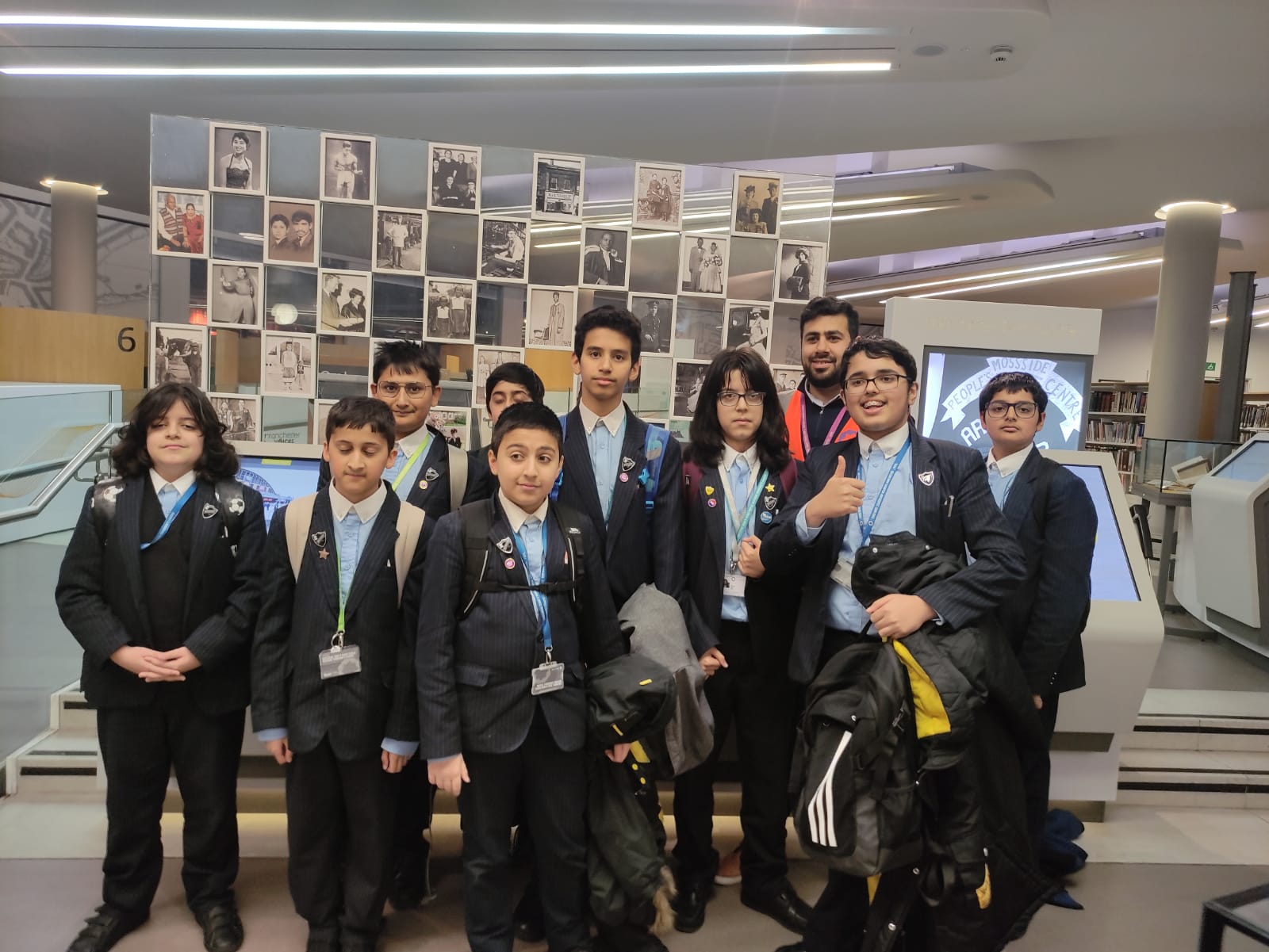 Group of schoolboys and a teacher pose for a photo in front of a black-and-white photo display in a library.