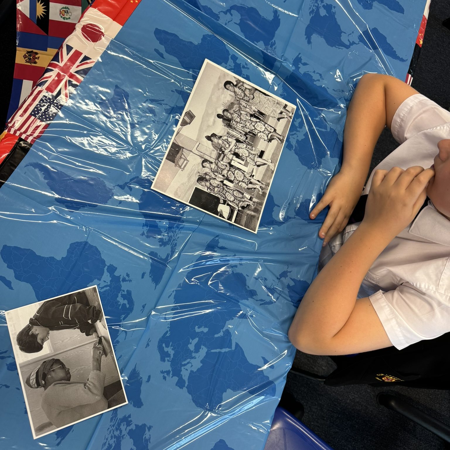 Child in school uniform views black-and-white archival photos on a blue world map-themed table cover.