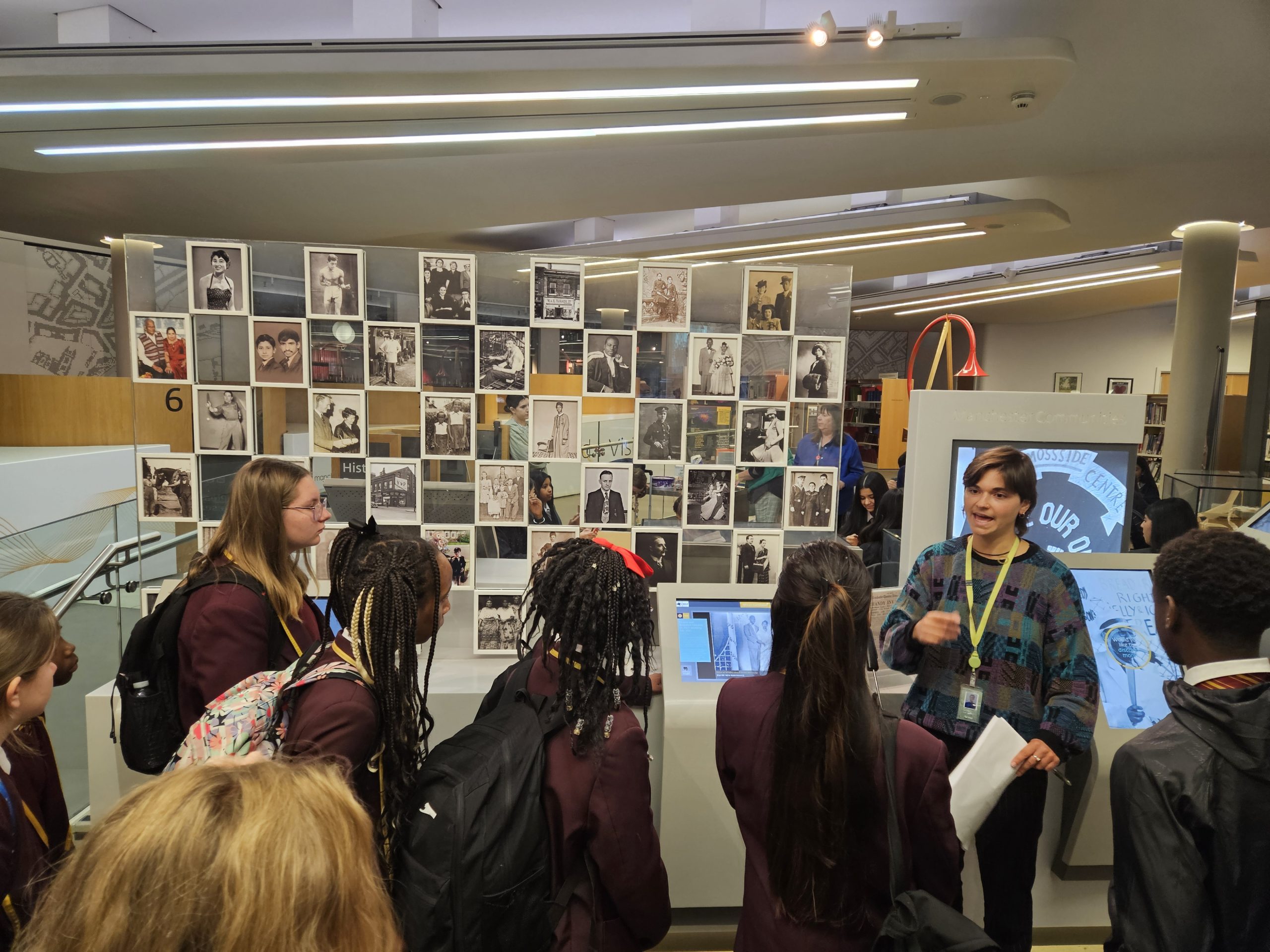Students gather around a photo wall exhibit as a guide explains images at the library’s heritage centre.